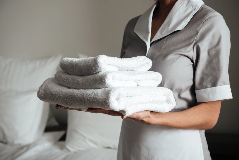 young hotel maid standing holding fresh clean towels